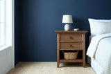 Iglesias rustic brown two-drawer nightstand with a ceramic lamp and a seagrass basket beside a bed in a Portland bedroom with a deep navy wall