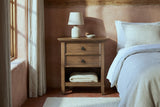 Iglesias rustic brown nightstand with a ceramic lamp and a folded wool blanket in a Santa Fe adobe bedroom with a terracotta plaster wall and a brick tile floor