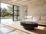 Imola Black Ash Oval Pedestal Coffee Table on a jute rug in front of a linen sofa in a poolside villa