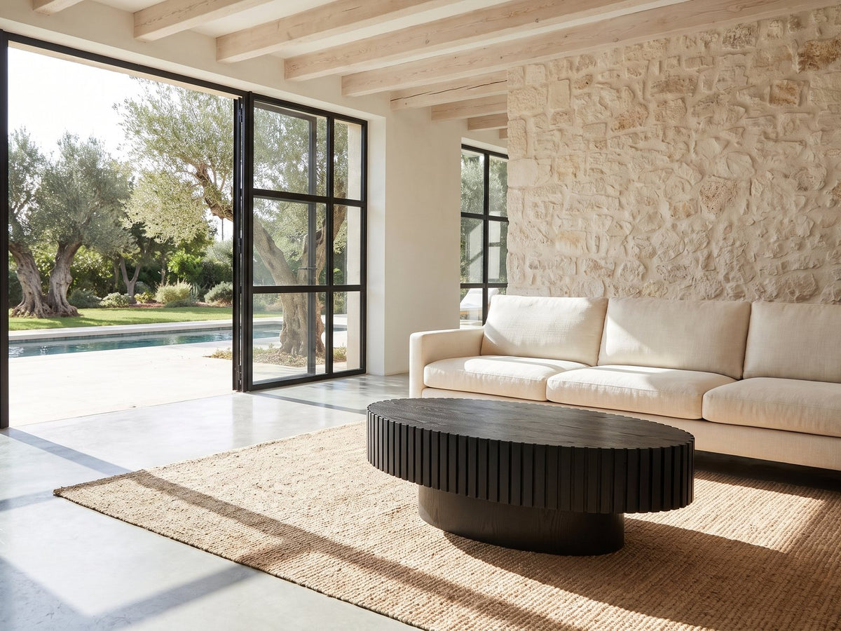 Imola Black Ash Oval Pedestal Coffee Table on a jute rug in front of a linen sofa in a poolside villa