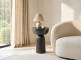 Irsina Cast Aluminum Tulip Pedestal Side Table with a lamp and a ceramic bowl beside a cream boucle armchair in a bright plaster room