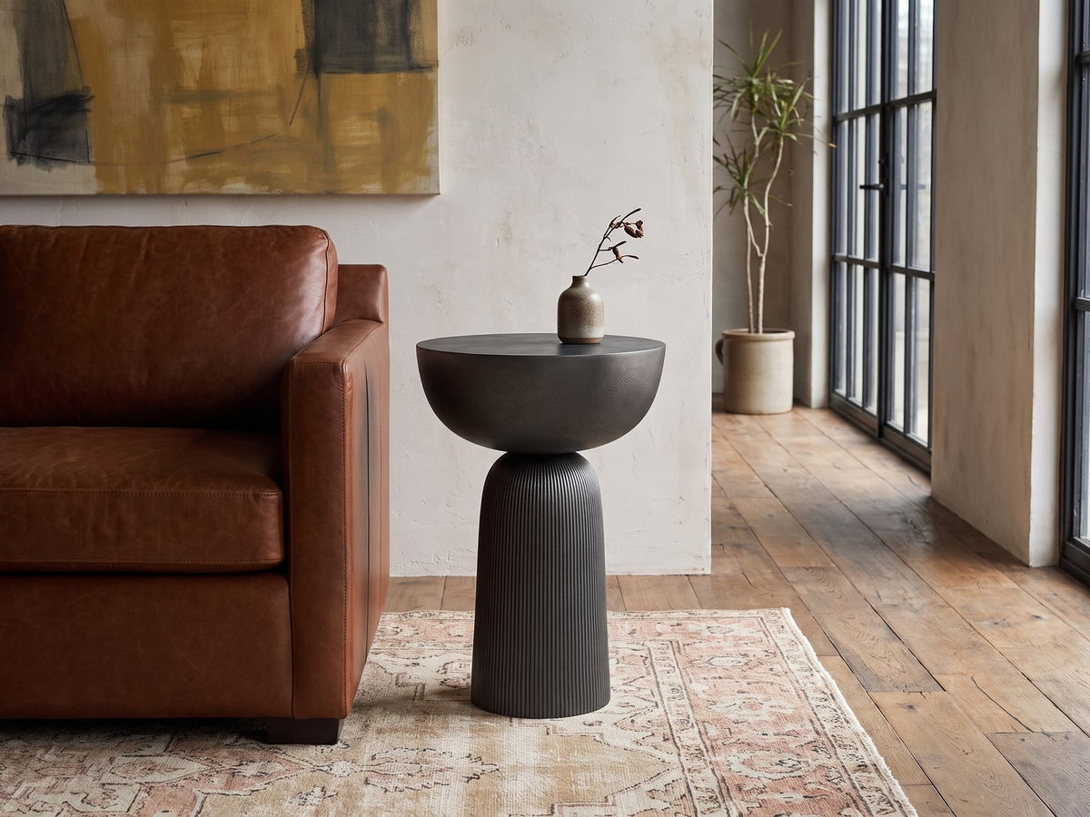 Irsina Cast Aluminum Tulip Pedestal Side Table beside a leather sofa in an industrial loft