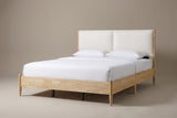 The Isernia bed in natural rubberwood with two cream cushions, a white mattress and pillows (not included), three-quarter view on a light studio backdrop