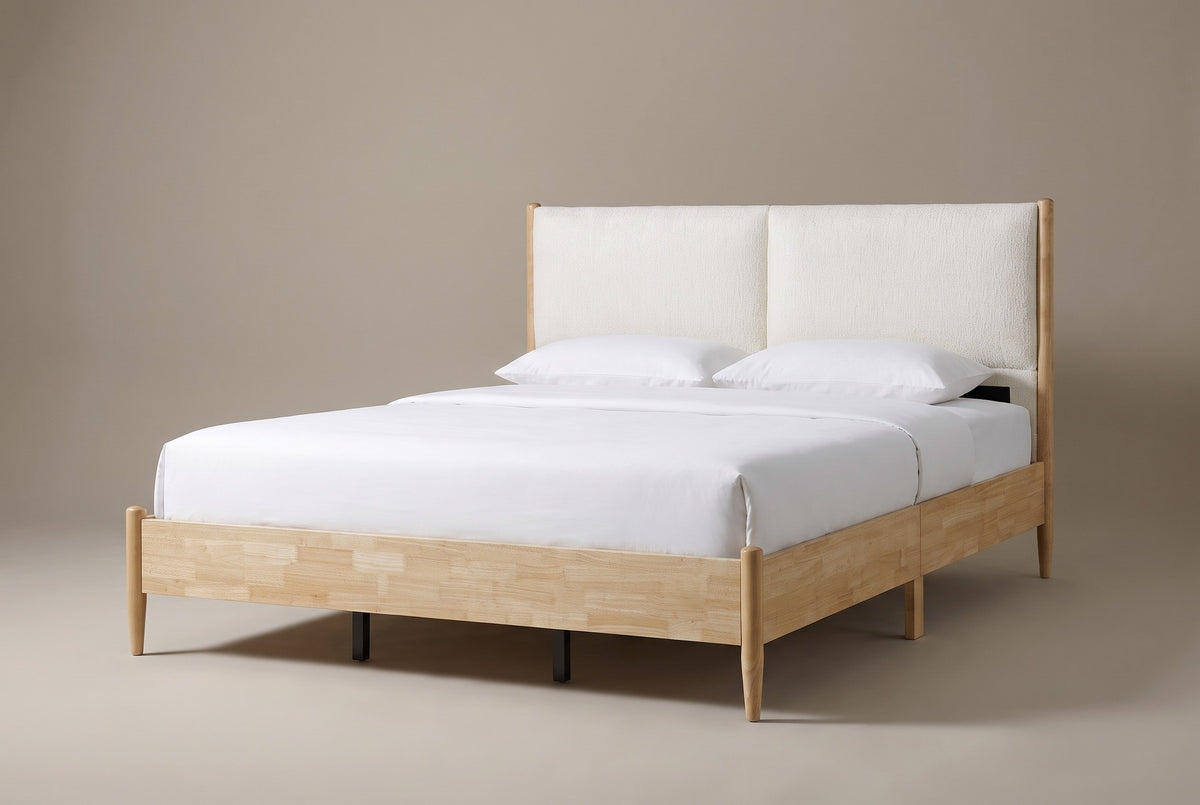 The Isernia bed in natural rubberwood with two cream cushions, a white mattress and pillows (not included), three-quarter view on a light studio backdrop