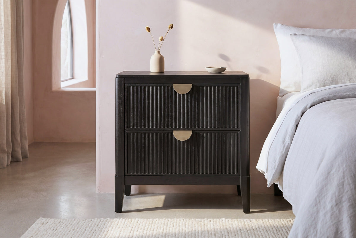 Isili black fluted nightstand against a blush pink limewash wall in a Palm Springs bedroom with a pale concrete floor and an arched window
