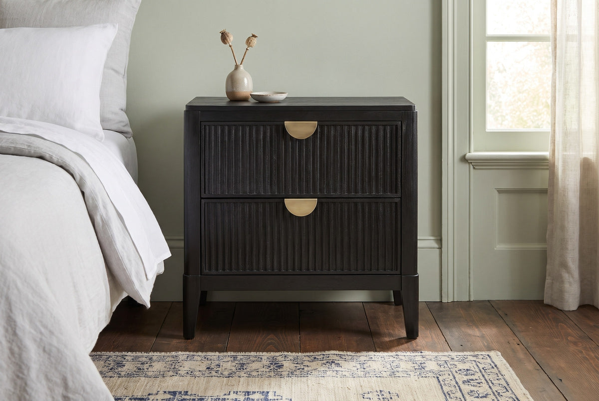 Isili black fluted nightstand against a pale sage green plaster wall in a Savannah bedroom with a dark heart pine floor