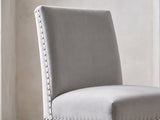 Close-up of the Itri 70-Inch White Marble Double Pedestal Dining Set with 6 Chairs: the tall flared back of a chair in light grey flannelette with silver nailhead trim