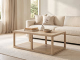 Ivrea Reclaimed Pine Open-Frame Coffee Table styled with books, a vase and a stone bowl in front of a cream sofa in a bright plaster room