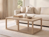 Ivrea Reclaimed Pine Open-Frame Coffee Table seen from the side, styled with books, a vase and a stone bowl in front of a cream sofa in a bright plaster room