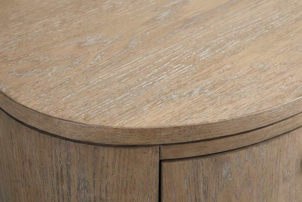Close-up of the Jerzu nightstand: wire-brushed toffee wood veneer with pale-filled pores along the edge of the oval top and the curved side below it