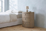 Jerzu cerused toffee oval nightstand with a ceramic lamp beside a bed in a Charleston bedroom with a pale blue-grey plaster wall and a pine floor
