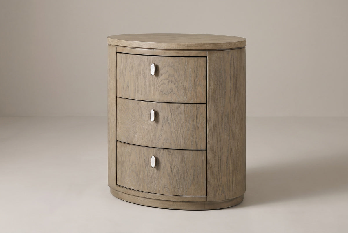 The Jerzu three-drawer oval nightstand in cerused toffee wood veneer, three-quarter view on a light studio backdrop