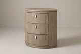 The Jerzu three-drawer oval nightstand in cerused toffee wood veneer, three-quarter view on a light studio backdrop