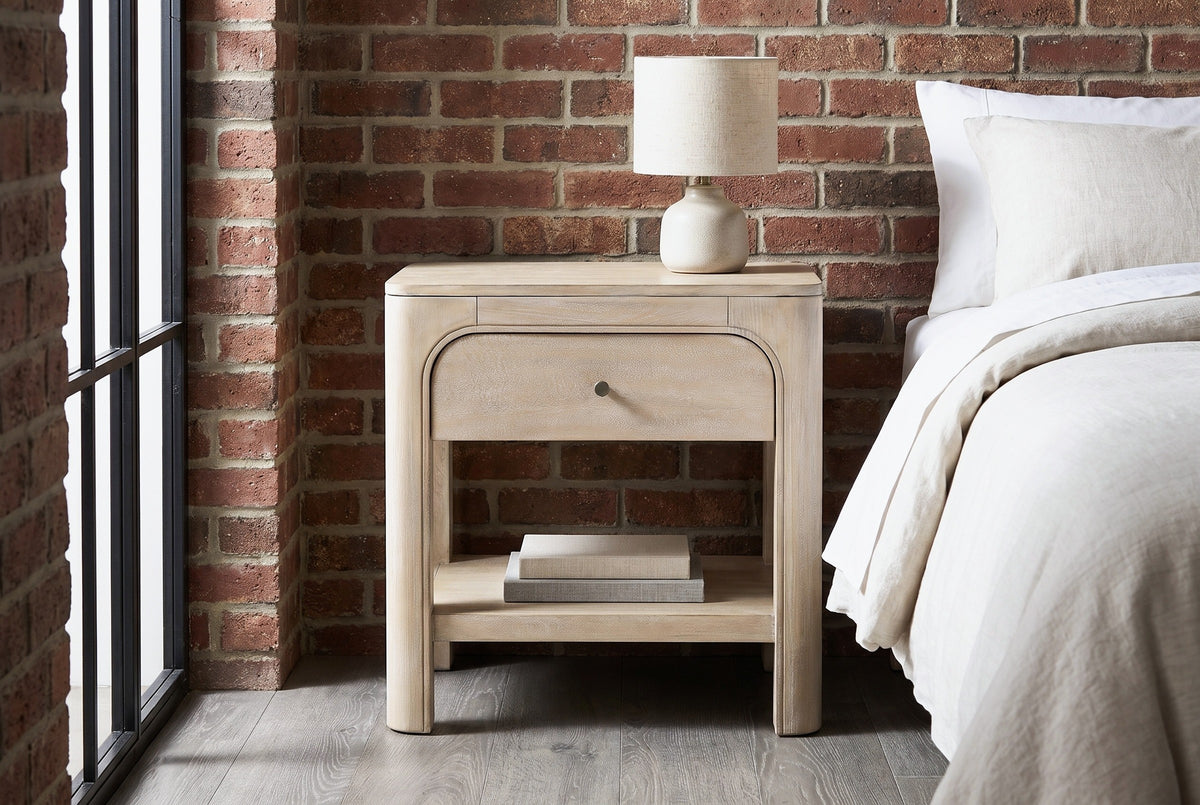 Laconi weathered mango arched nightstand against an exposed red-brown brick wall in a Brooklyn loft bedroom with a black steel window and a grey oak floor