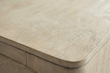 Close-up of the weathered mango on the Laconi nightstand: a pale sandy wood with fine rippled grain and a light white wash, at the rounded corner of the top
