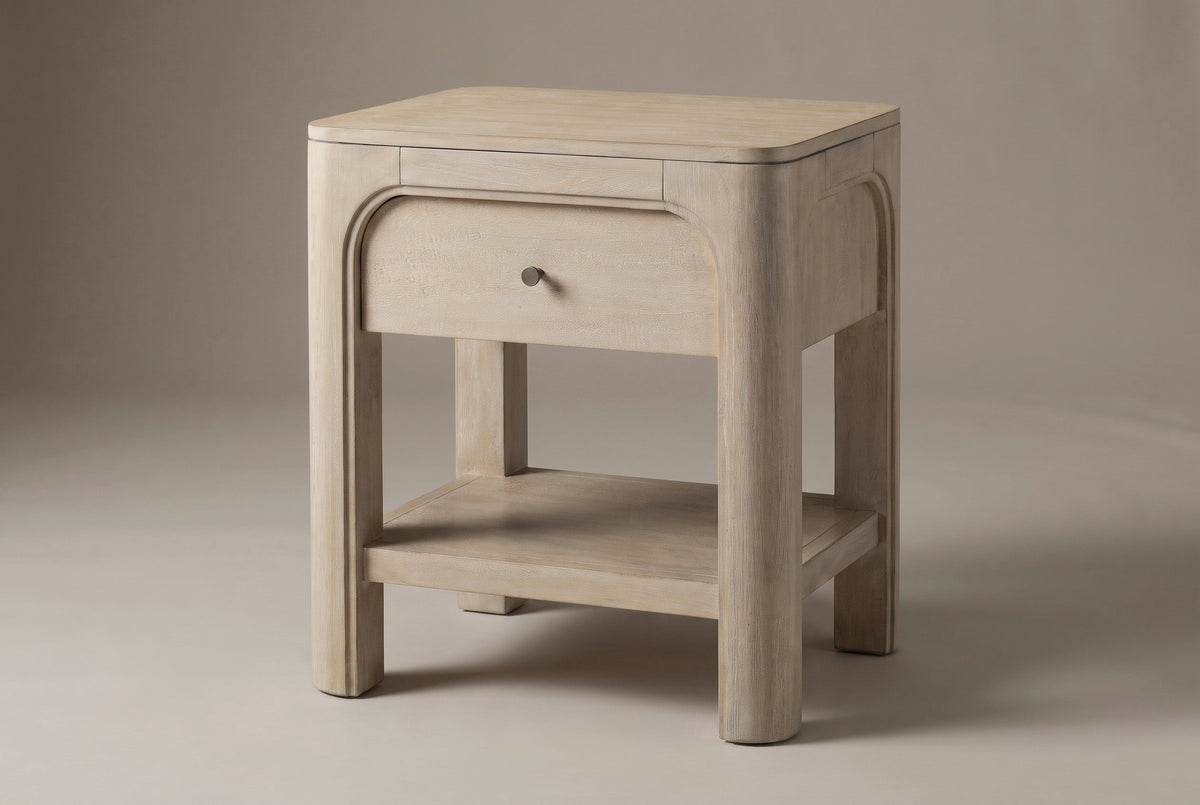 The Laconi nightstand in weathered mango with one drawer inside a raised arch, a bronze-tone knob, an open lower shelf and four chunky rounded posts, three-quarter view on a light studio backdrop