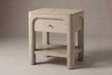The Laconi nightstand in weathered mango with one drawer inside a raised arch, a bronze-tone knob, an open lower shelf and four chunky rounded posts, three-quarter view on a light studio backdrop