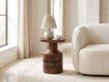 Lagonegro Solid Mango Pedestal Side Table with a lamp and a ceramic bowl beside a cream boucle armchair in a bright plaster room