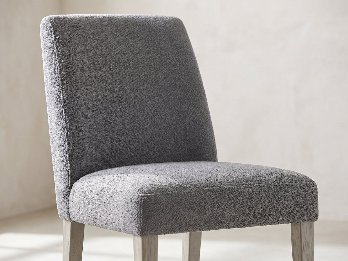 Close-up of the Laino 82-Inch Racetrack Oak Double Pedestal Dining Set with 4 Chairs: the tall upholstered back and padded seat of a chair in grey boucle