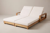 The Lampedusa double chaise lounge in light natural acacia with two cream four-fold cushions, both backrests raised, three-quarter view on a light studio backdrop