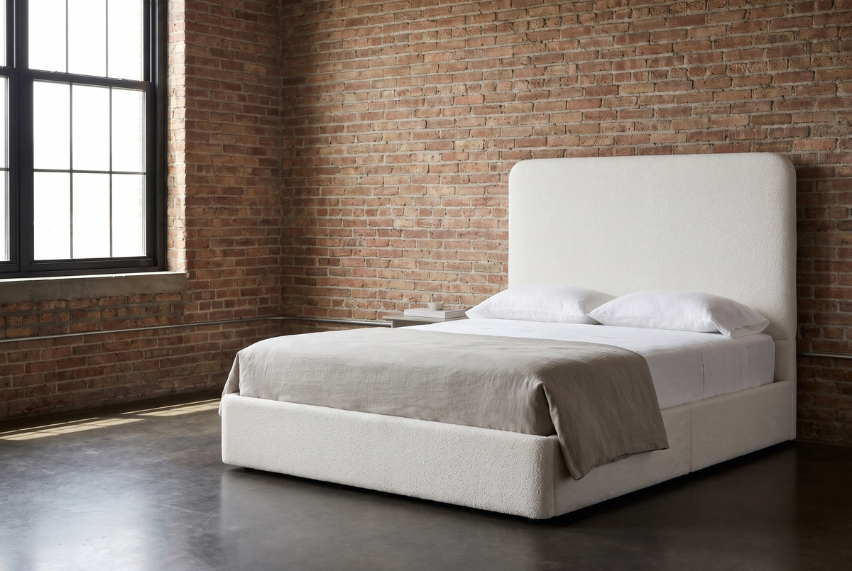 Lanciano pearl white chenille bed against an old red-brown brick wall in a Chicago loft bedroom, a tall black steel window at the left
