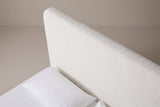The top corner of the Lanciano headboard: a thick padded pearl white panel with a generously rounded corner, above a white pillow