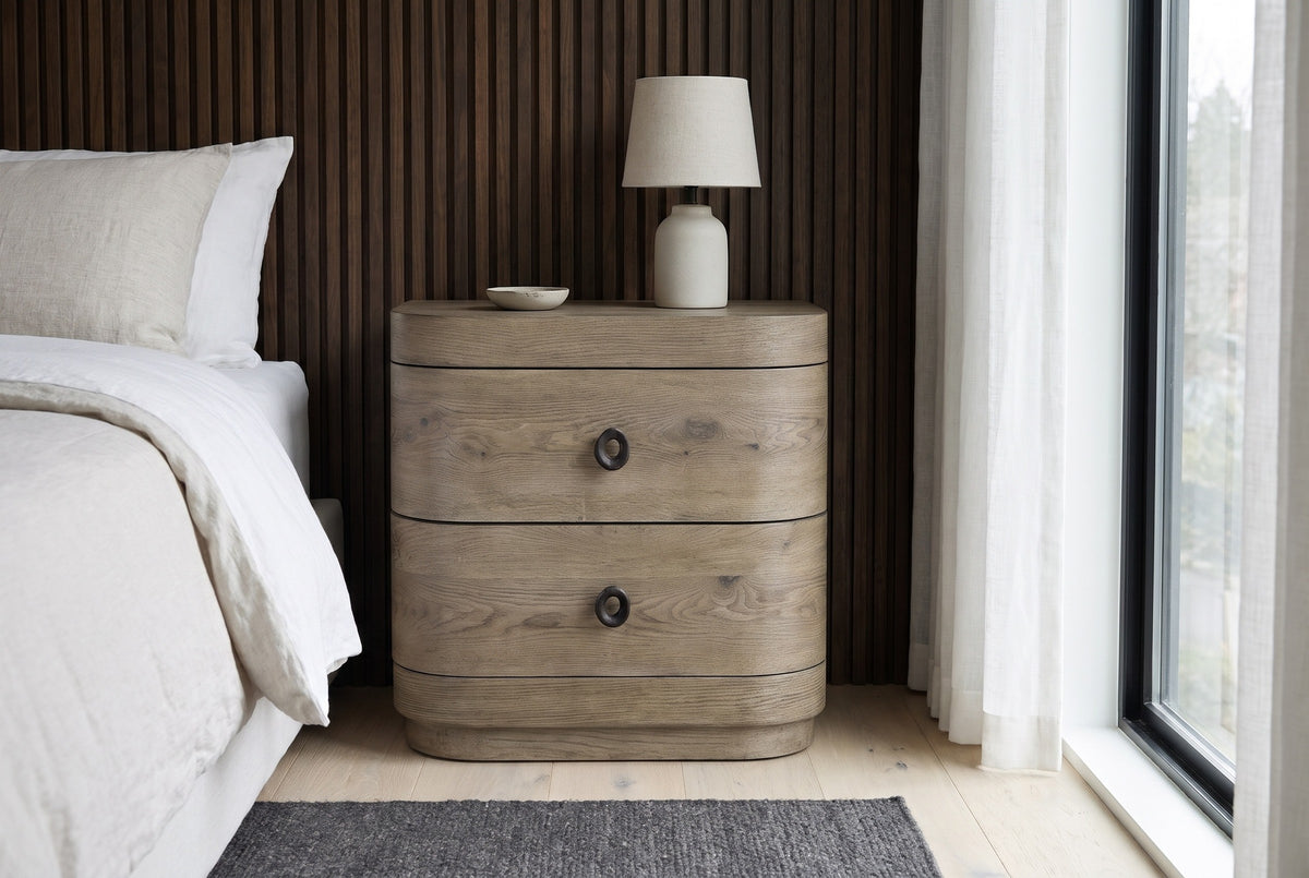 Lanusei knotty oak nightstand with a ceramic lamp against dark walnut slat panelling in a Seattle bedroom with a pale oak floor, a charcoal rug and a tall window