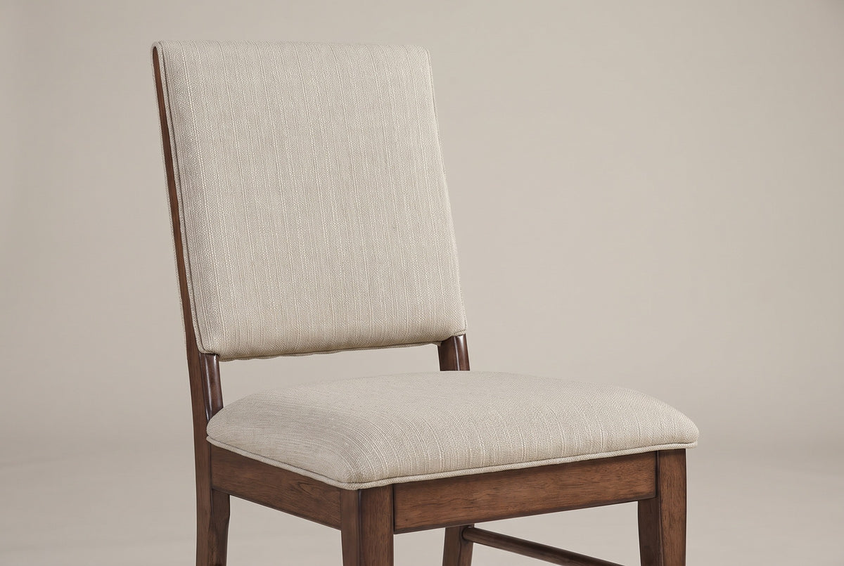 A Lavello chair close up: the square upholstered back with a thin piped edge, the open gap above the padded seat, and the wooden frame