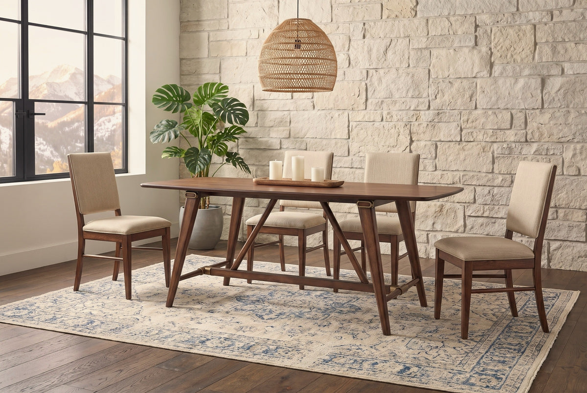 Lavello walnut trestle dining table with four upholstered chairs against a pale limestone block wall in a Denver dining room with a rattan pendant light and mountain view