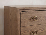 Close-up of the Legnago 40-Inch Latte Elm 5-Drawer Chest: an antique-brass ring pull, the rounded corner of the drawer stack and the mitred frame