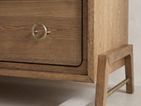 Close-up of the Lendinara 66-Inch Latte Elm 6-Drawer Dresser: a brass ring pull and a splayed solid-wood leg with its brass stretcher