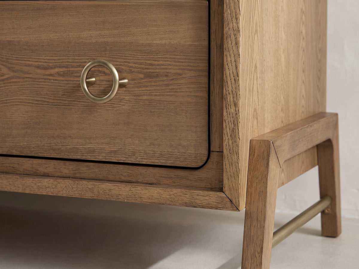 Close-up of the Lendinara 66-Inch Latte Elm 6-Drawer Dresser: a brass ring pull and a splayed solid-wood leg with its brass stretcher