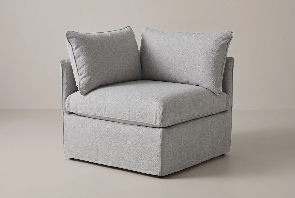 The Lentini slipcovered corner chair in light grey, three-quarter view from the front on a light studio backdrop