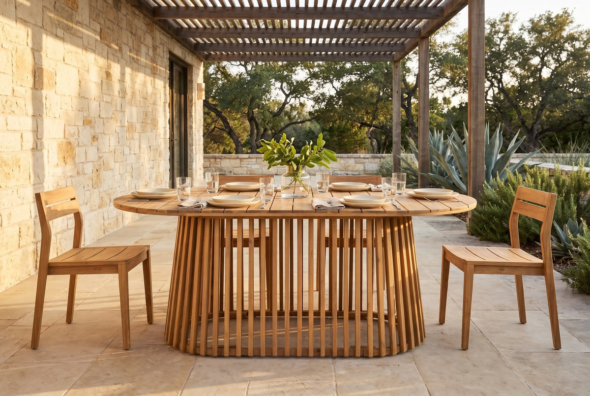 Levanzo oval acacia dining table on a limestone terrace in the Texas Hill Country at golden hour, a cedar pergola and live oaks behind (chairs, tableware and flowers not included)