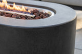 Close-up of the dark grey concrete on the Licata fire pit table: the rounded end and rim beside the stainless burner pan, volcanic rock and the end of the flame