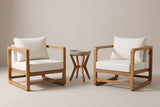 The Linosa set: two acacia lounge chairs with white cushions and a round concrete side table between them, on a light studio backdrop