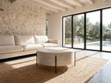 Lucignano Whitewashed Mango Drum Coffee Table on a jute rug in front of a linen sofa in a poolside villa