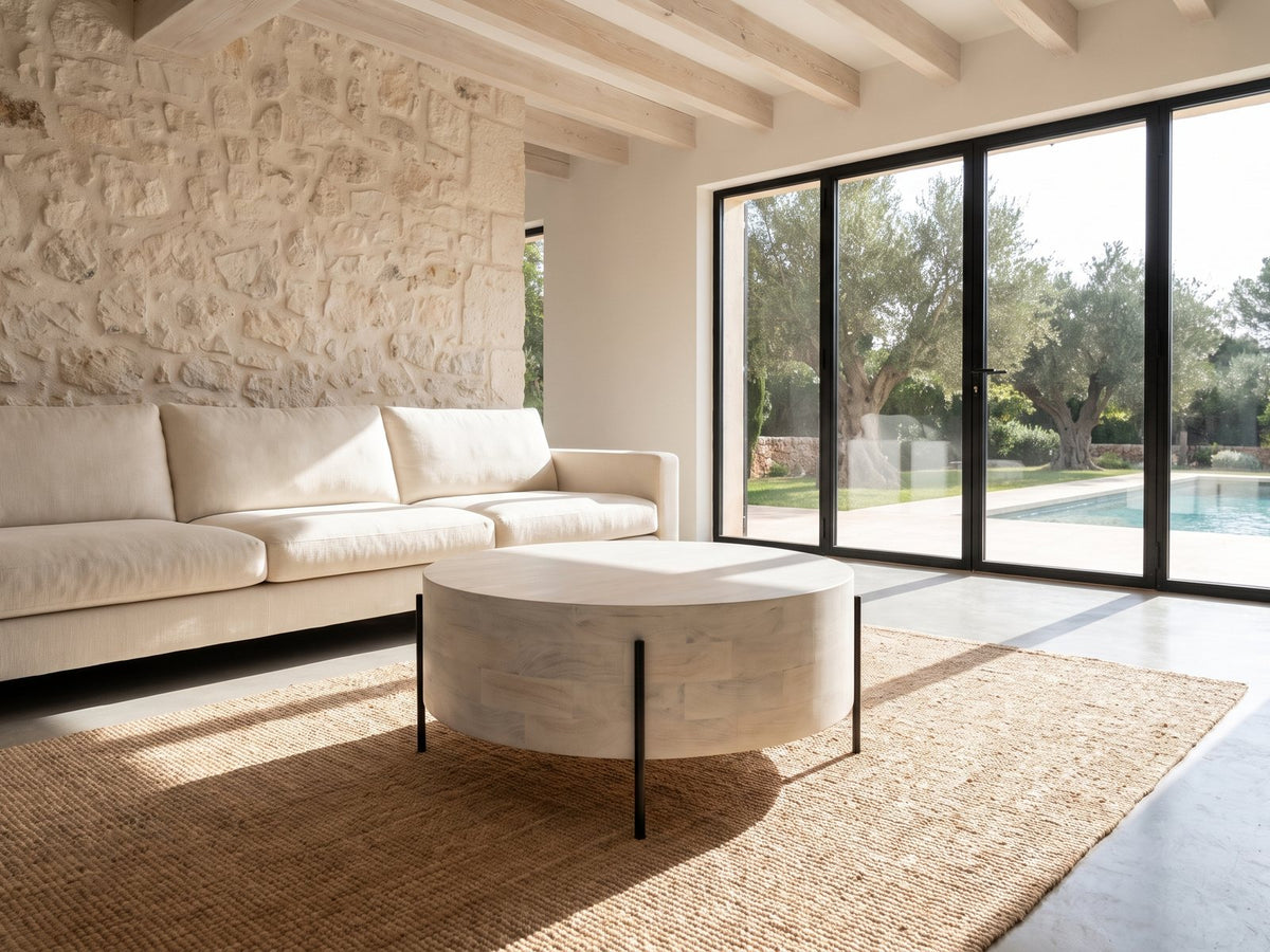 Lucignano Whitewashed Mango Drum Coffee Table on a jute rug in front of a linen sofa in a poolside villa