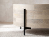 Close-up of the Lucignano Whitewashed Mango Drum Coffee Table: a black metal rod leg rising along the whitewashed mango drum