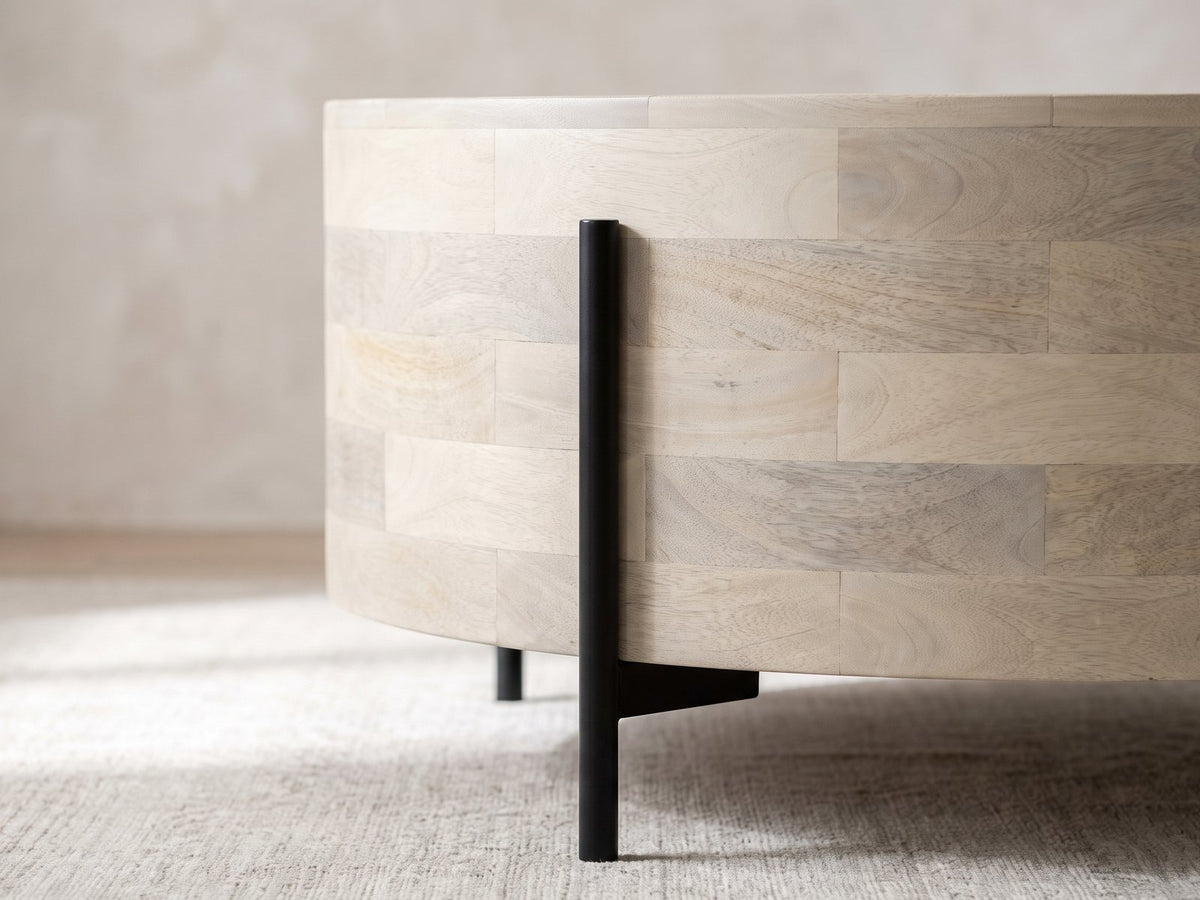 Close-up of the Lucignano Whitewashed Mango Drum Coffee Table: a black metal rod leg rising along the whitewashed mango drum