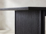 Close-up of the Lungro 82-Inch Reeded Black Oak Extension Dining Set with 4 Chairs: the reeded slab leg under the bevelled edge of the black oak top