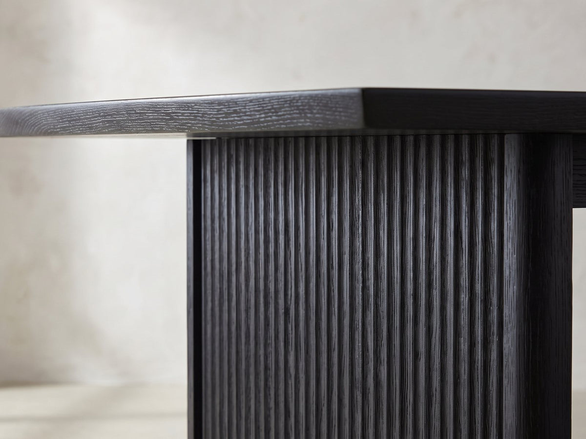 Close-up of the Lungro 82-Inch Reeded Black Oak Extension Dining Set with 4 Chairs: the reeded slab leg under the bevelled edge of the black oak top