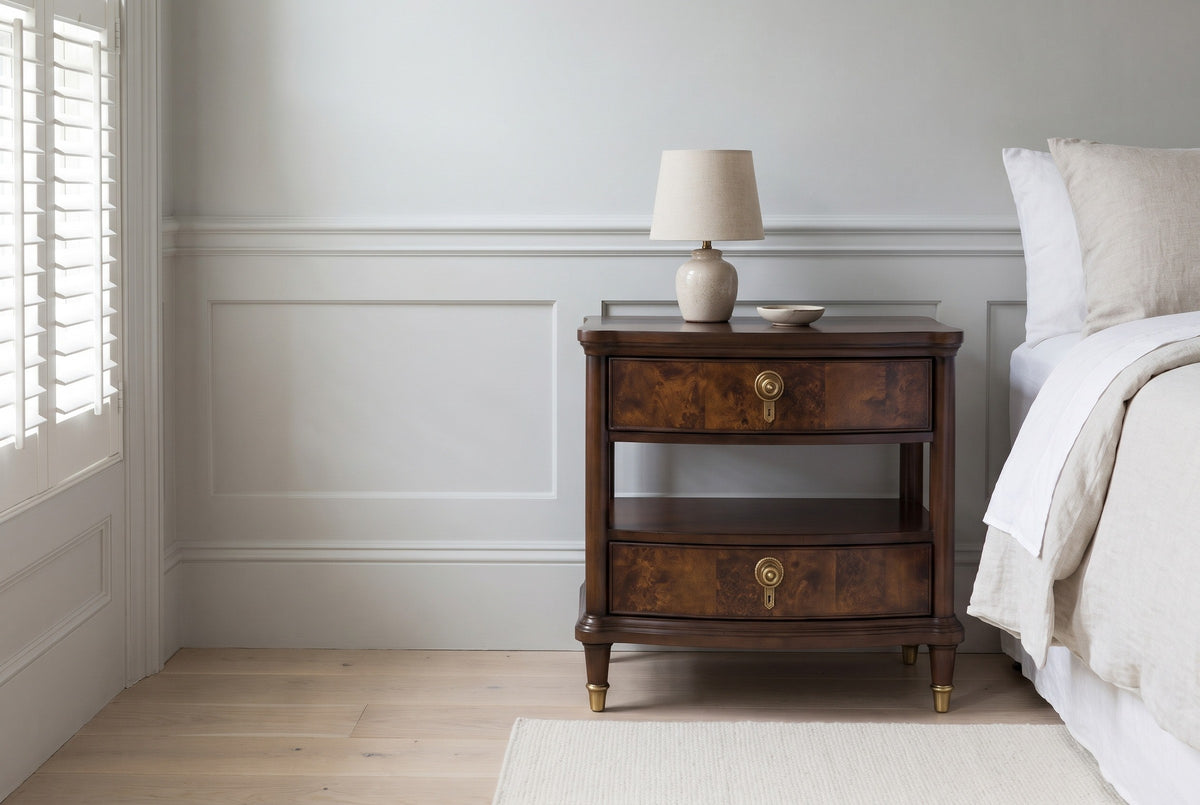 Luras dark cherry and burl nightstand with a ceramic lamp beside a bed in a Boston Back Bay bedroom with pale dove-grey wainscot panelling, a shuttered window and a pale oak floor