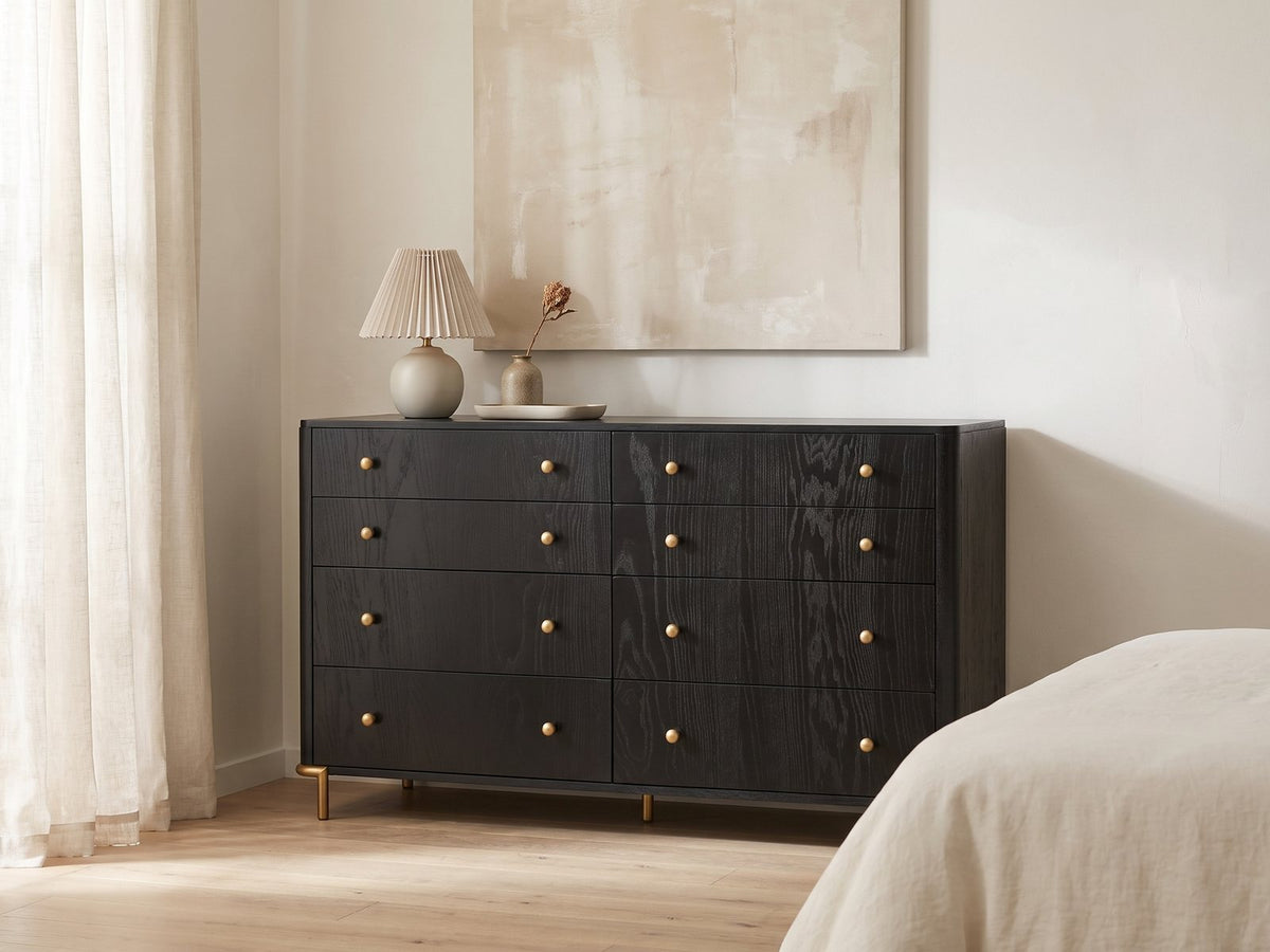 Malcesine 63-Inch Wire-Brushed Black 8-Drawer Dresser against a plaster wall under an abstract canvas in a bright bedroom