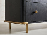 Close-up of the Malcesine 63-Inch Wire-Brushed Black 8-Drawer Dresser: the soft-gold metal sled under one end, the rod curving round the corner into a slim round leg
