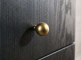 Close-up of the Malcesine 63-Inch Wire-Brushed Black 8-Drawer Dresser: a round soft-gold ball knob on the black wire-brushed grain of a drawer front