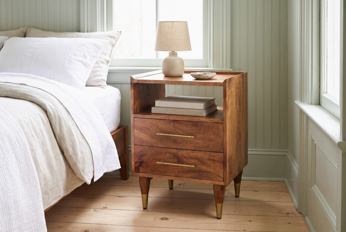 Mamoiada golden-brown mango nightstand with a ceramic lamp and two books in the cubby in a Charleston bedroom with pale sage green beadboard walls and pine floorboards