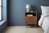 Mamoiada golden-brown mango nightstand against a deep slate blue plaster wall in a Minneapolis bedroom with pale oak floorboards
