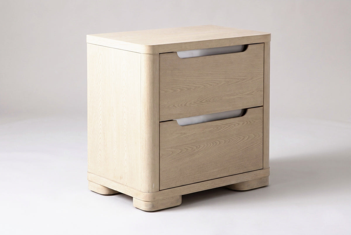 The Mandas nightstand in light elm veneer with two drawers, brushed nickel scoop pulls and low rounded feet, three-quarter view on a light studio backdrop