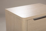 The top corner of the Mandas nightstand: a thick light elm top with a rounded front corner, the rounded corner post and the end of a nickel-lined scoop on the upper drawer